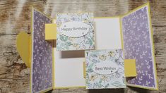 an open birthday card with yellow and purple flowers on it, sitting on a wooden table