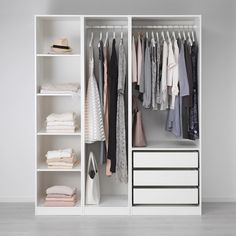 an open white closet with clothes hanging on the shelves and drawers in front of it