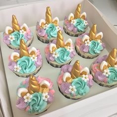 cupcakes decorated with pastel frosting and gold unicorn hats are displayed in a box