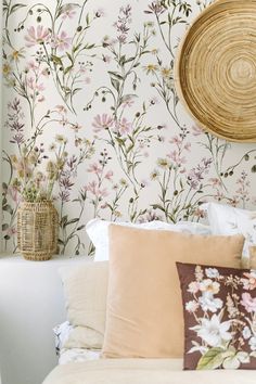 a white bed topped with lots of pillows next to a wall covered in floral wallpaper