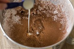 someone is mixing chocolate in a bowl with a measuring spoon on the side and powdered sugar being poured into it