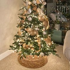 a christmas tree with gold and silver ornaments in a basket on the floor next to a couch