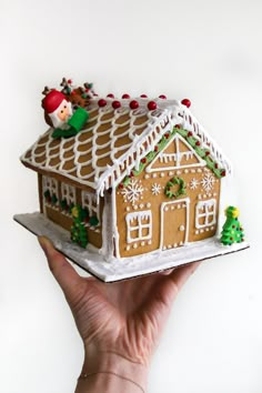 a gingerbread house with icing and decorations on it is being held by a hand