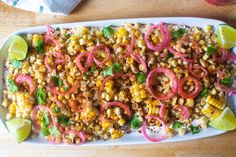 a platter filled with corn, onions and cilantro on top of a wooden table