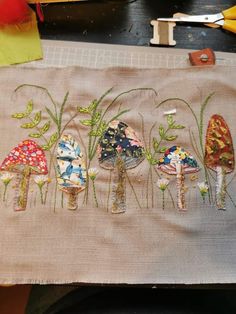 a piece of cloth with embroidered images of mushrooms on it and scissors in the background