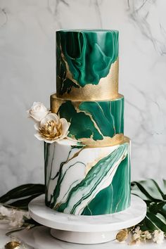 a three tiered green and gold marble cake with flowers on the top, surrounded by greenery