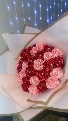 a bouquet of red and pink roses in a paper wrapper with string lights behind it