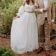 a man and woman standing next to each other in front of some bushes with flowers