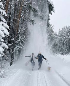 two people are walking through the snow in front of a waterfall