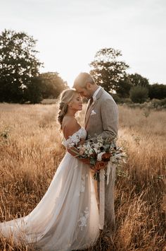 a bride and groom standing in the middle of a field with tall grass at sunset