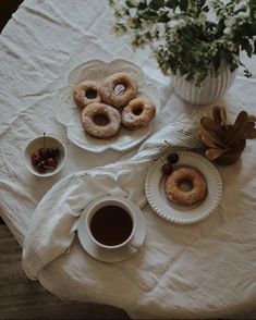 donuts and coffee on a white tablecloth with flowers in a vase behind them