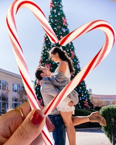 two people holding candy canes in front of a christmas tree