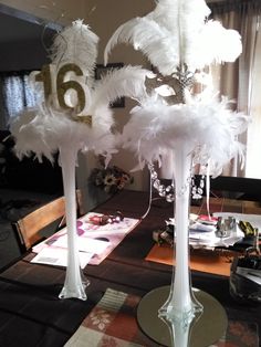 two tall white vases sitting on top of a table covered in feathers and numbers