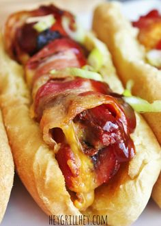 two hot dogs on buns with bacon and relish sitting next to each other