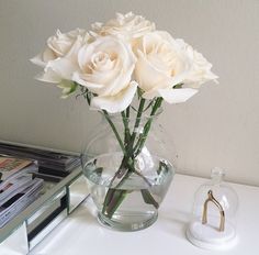 some white roses in a clear vase on a table next to a stack of books