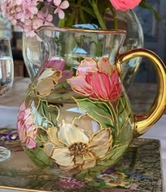 a glass pitcher with flowers painted on it sitting on a table next to wine glasses