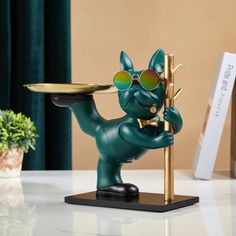 a green cat figurine with sunglasses holding a tray