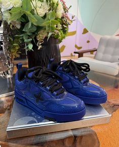 a pair of blue sneakers sitting on top of a table next to a vase with flowers