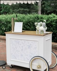 a white cart with flowers and pictures on the top is sitting outside in front of some bushes