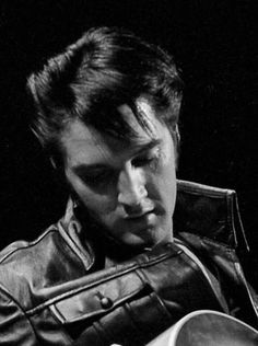 a man with a guitar in his hand and wearing a leather jacket is looking at the camera