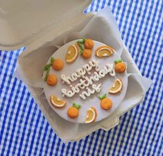 a decorated birthday cake in an open box on a blue and white checkered tablecloth