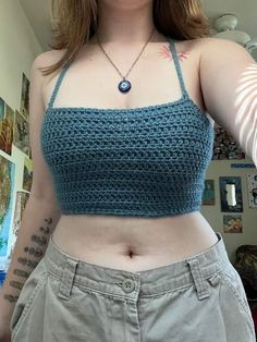 a woman wearing a blue crochet crop top and khaki pants with tattoos on her arm