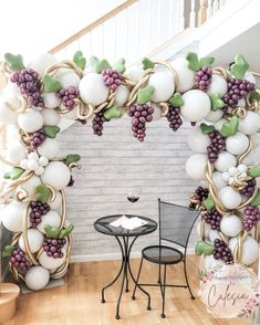 a table and chairs in front of a large balloon arch with grapes hanging from it