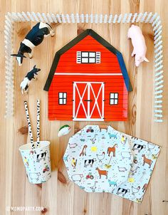 farm animals and barn decorations on a wooden table with paper cups, forks and napkins