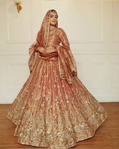 a woman in a red and gold bridal gown standing on a wooden floor with her hands behind her head