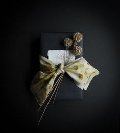 a wrapped gift with dried flowers on it and a ribbon tied around the top, sitting on a black surface