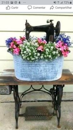 an old sewing machine is sitting on a small table with flowers in it and a potted planter