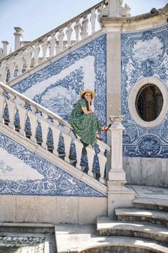 a woman in a green dress and straw hat is standing on the steps of a blue tiled building