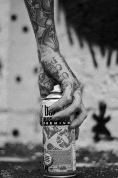 a person holding onto a can of beer with tattoos on their arm and hand, in front of a brick wall