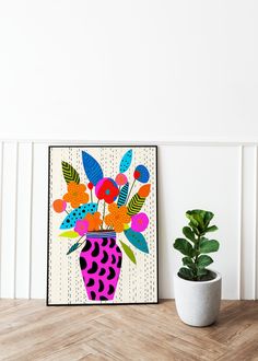 a potted plant sitting next to a painting on a wooden table in front of a white wall