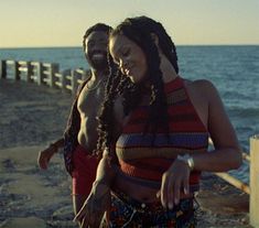 two people are standing on the beach by the water and one is holding something in her hand