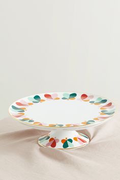 an empty plate with multicolored circles on the rim sits on a white surface