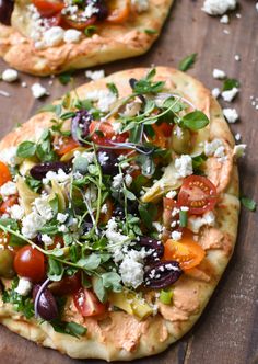 two flatbread pizzas topped with fresh veggies and feta cheese on a wooden board