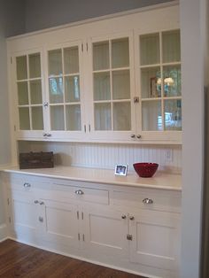 an empty kitchen with white cabinets and wood flooring, along with a red bowl on the counter