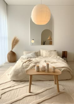 a white bed sitting in a bedroom next to a mirror and table with candles on it