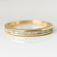 a gold wedding band with white opal inlaying the side, on a white surface