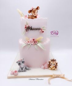 a three tiered pink cake with animals on top and flowers around the bottom layer