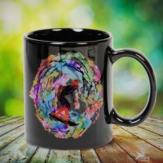 a black coffee mug with an abstract painting on the outside and inside, sitting on a wooden table