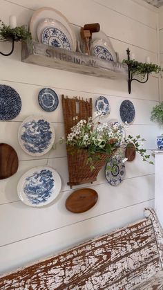 blue and white plates hang on the wall next to a bench with flowers in it