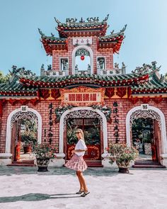 a woman standing in front of a red brick building with chinese decorations on it's roof