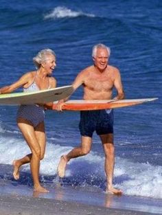 an older man and woman walking on the beach with their surfboards in hand,