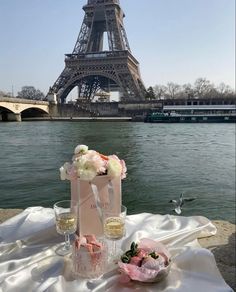 the table is set with champagne and flowers near the water in front of the eiffel tower