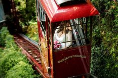 a red trolley car with people in it going down the tracks and trees behind it