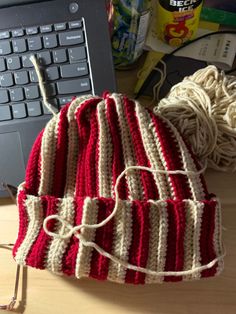 a red and white knitted hat sitting on top of a table next to a laptop computer