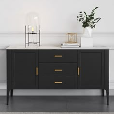 a black and white sideboard with two vases on top of it next to a plant