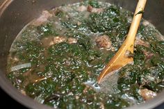 a pot filled with meat and spinach in broth next to a wooden spoon